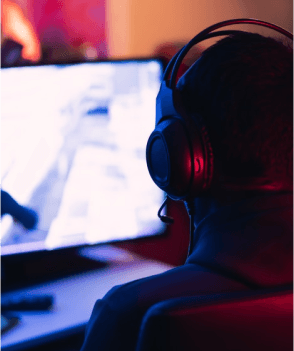 A man is wearing headphones with his back to the camera looking at something on his computer monitor that's unclear.