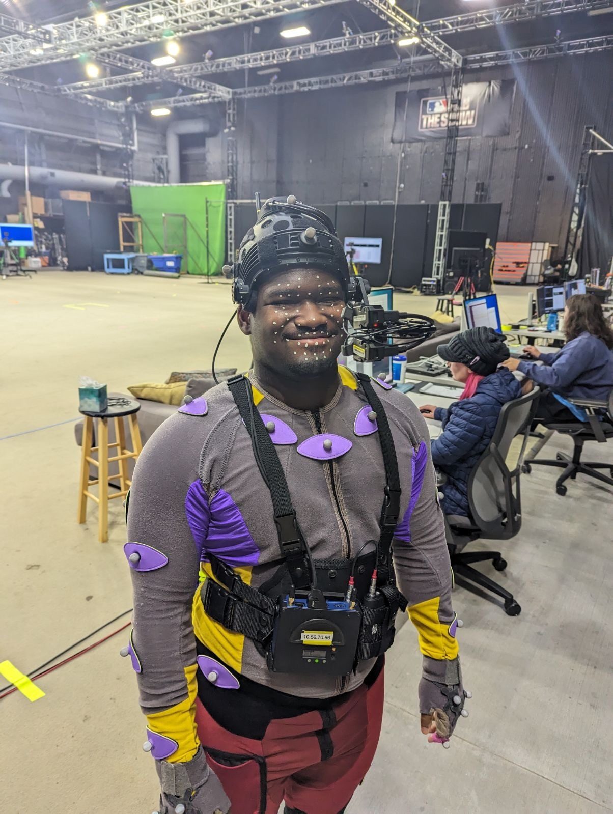 A young man wearing motion capture gear, standing in a large concrete studio.