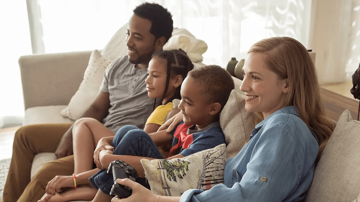 母親、二人の息子、父親がソファに並んで座り、テレビ画面に向かって一緒にゲームをしている