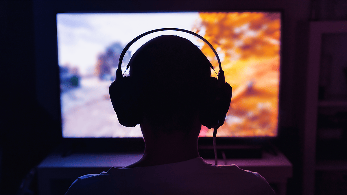 男性がカメラに背を向けてヘッドホンを装着し、テレビ画面に映る何かを見ている。