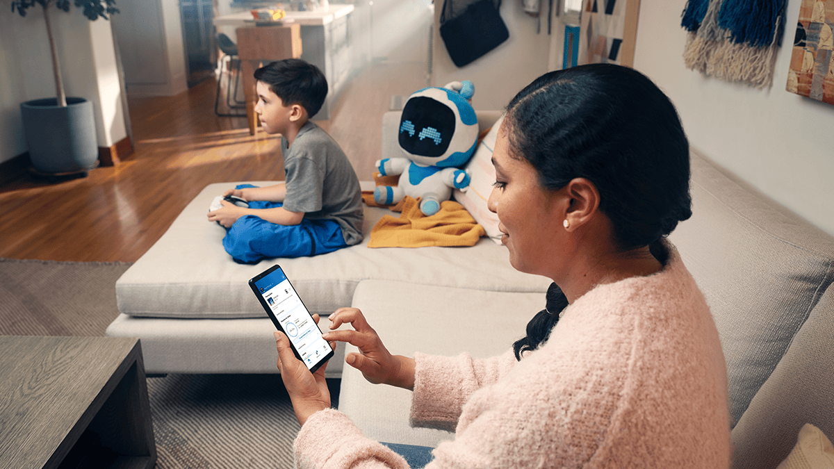 保護者がスマホでPlayStation Familyアプリを閲覧している様子。子どもが隣でゲームをプレイしている。