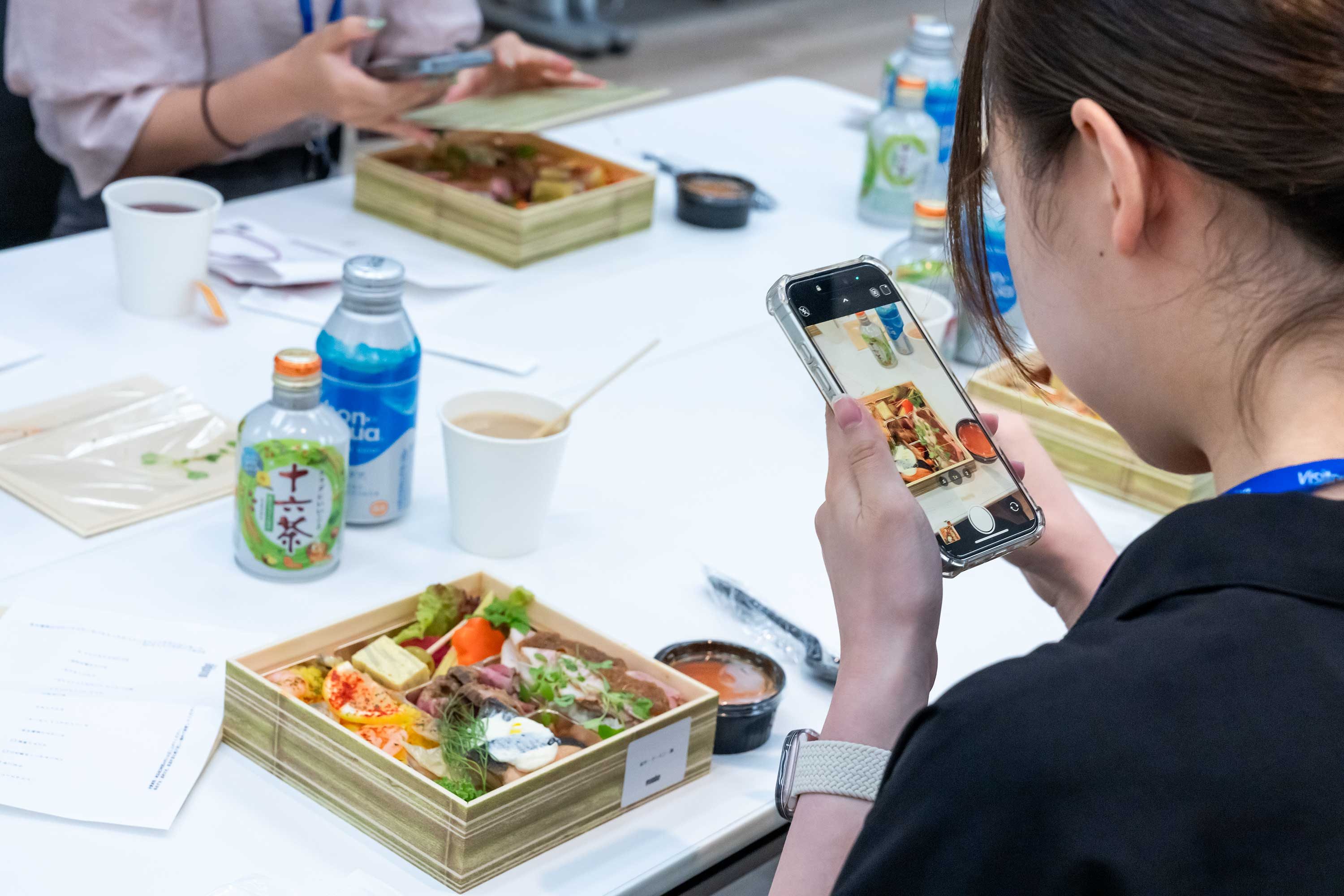 お昼のお弁当をスマートフォンで撮影しているイベントの参加者