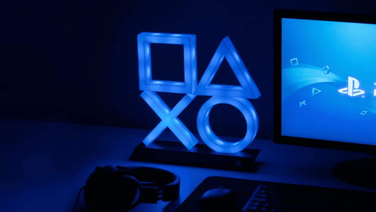 暗い部屋の中で、プレイステーションのシェイプス（四角、三角、バツ、丸）でできたライトが青く光っている。その横にはプレイステーションの背景を映したモニター。