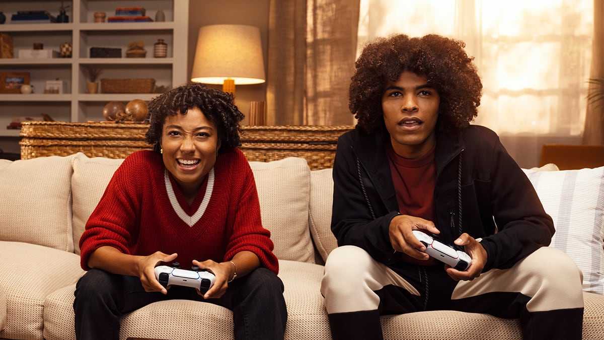 ソファに並んで座り、PlayStationコントローラーで一緒にゲームをプレイする2人の若者。