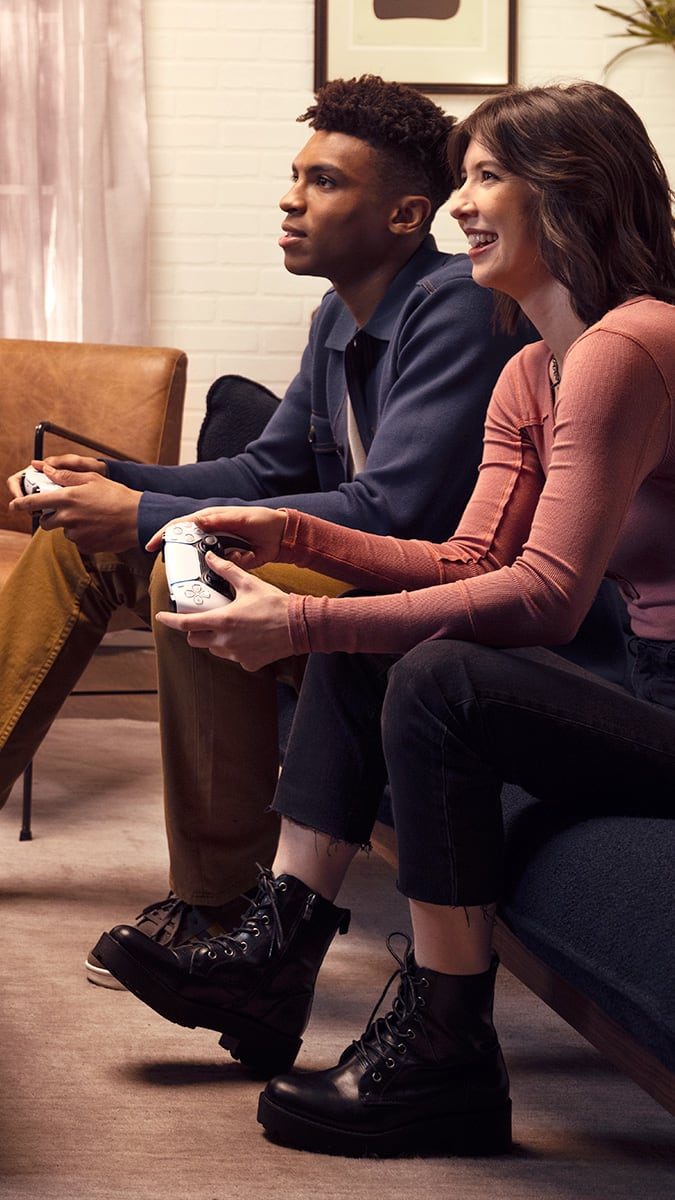 ソファに座り、DualSense コントローラーで笑顔でゲームを楽しむ男女を横から捉えたショット。